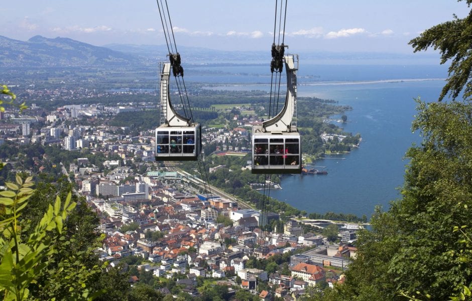 Blick vom Pfänder auf die talwärts und bergwärts fahrenden Kabinen der Pfänderbahn und auf die Stadt Bregenz am Bodensee.