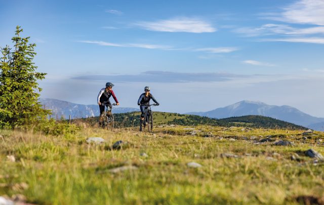 Eine Mountainbikerin und ein Mountainbiker auf einem Weg in einer Wiese in einer gemäßigt hügeligen Landschaft. (c) Erlebnisarena St. Corona am Wechsel