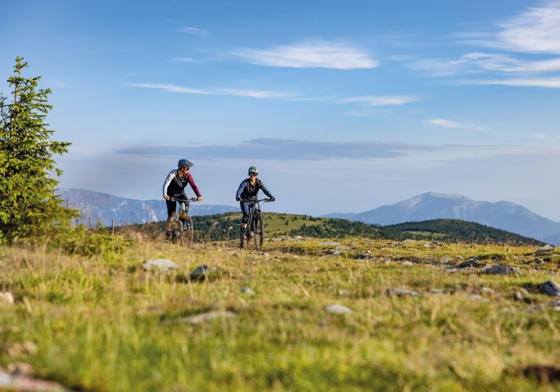 Eine Mountainbikerin und ein Mountainbiker auf einem Weg in einer Wiese in einer gemäßigt hügeligen Landschaft. (c) Erlebnisarena St. Corona am Wechsel