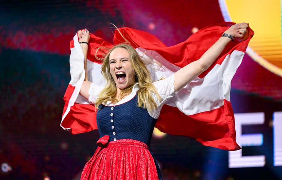 Rezeptionistin Elena Mathis freut sich über ihre Goldmedaille bei den EuroSkills 2025 und schwingt die österreichische Fahne.