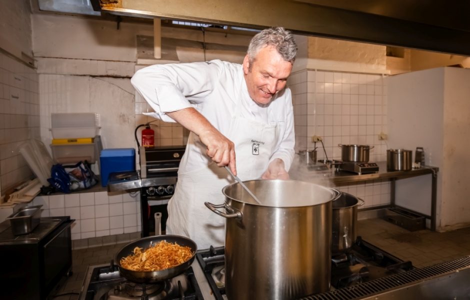 Koch Wolfgang Mätzler rührt lächelnd in einem großen Topf.
