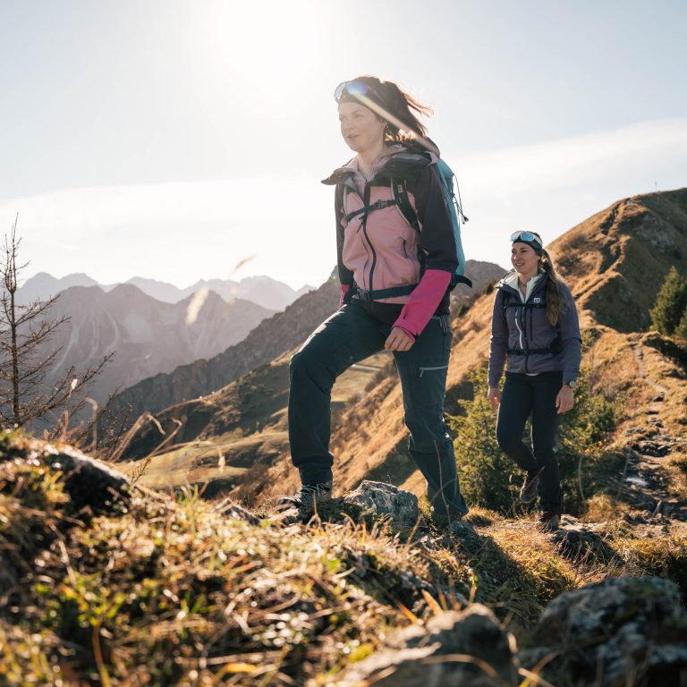 Zwei Frauen wandern in der herbstlichen Bergwelt des Kleinwalsertals.