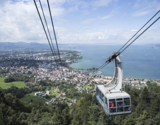Blick von der Bergstation der Pfänderbahn auf eine Gondeln, die Stadt Bregenz und den Bodensee.