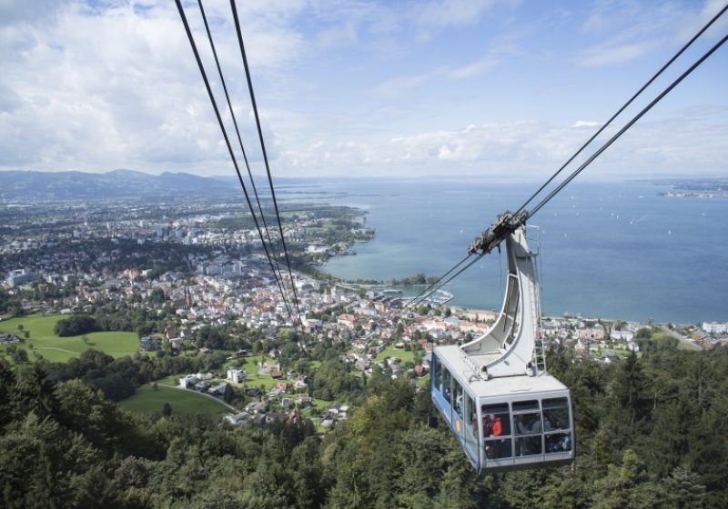 Blick von der Bergstation der Pfänderbahn auf eine Gondeln, die Stadt Bregenz und den Bodensee.