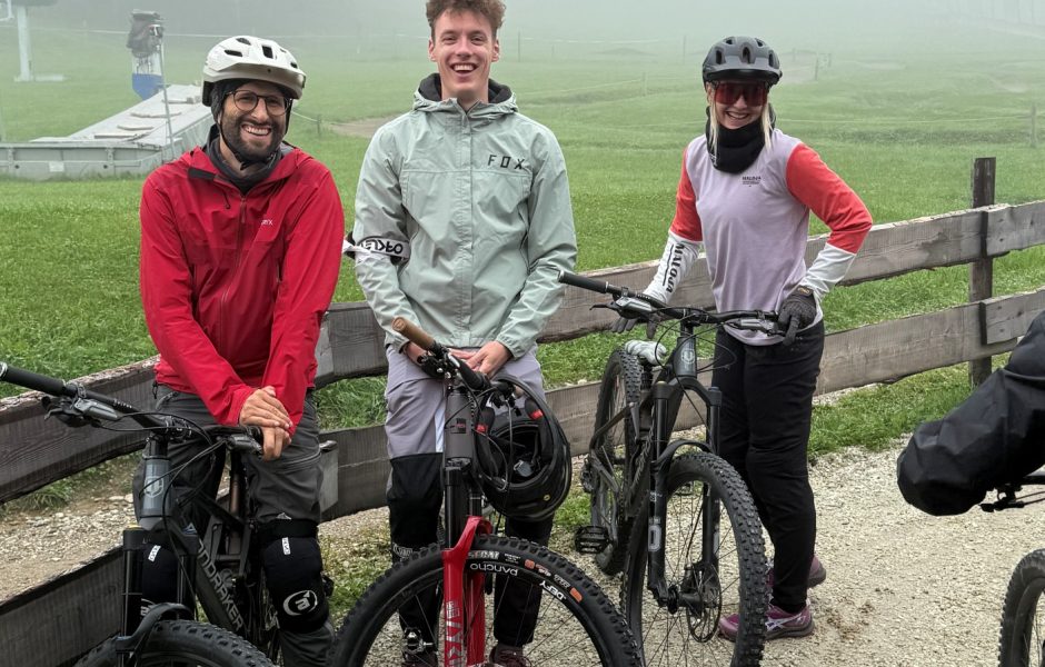 Drei Personen in Mountainbike-Ausrüstung stehen mit ihren Mountainbikes vor einer nebligen Kulisse.