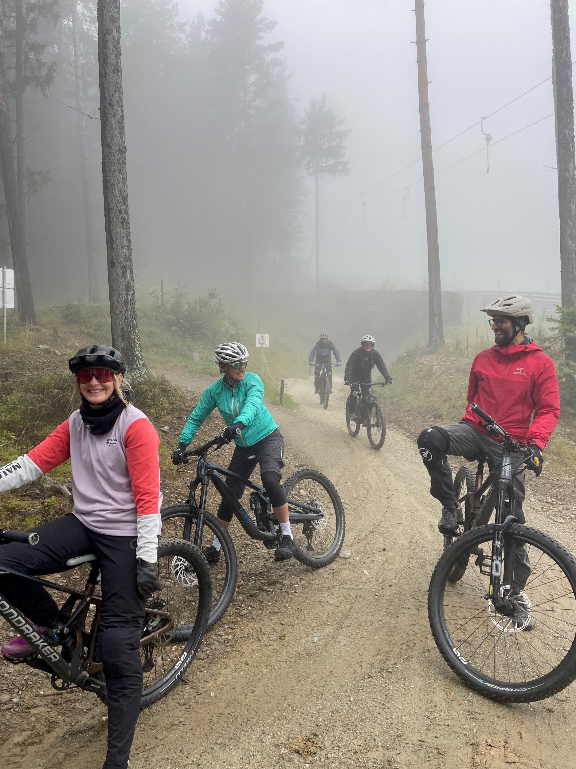 Mehrere Mountainbiker:innen stehen auf einer Strecke im Wald.