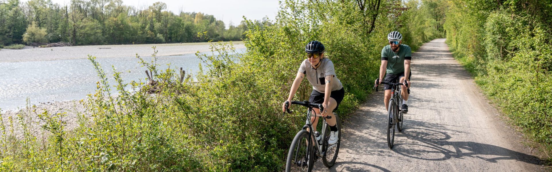 Zwei Gravelbiker - eine Frau und ein Mann - fahren mit Gravelbikes der Bregenzerach entlang, beide tragen einen Fahrradhelm.