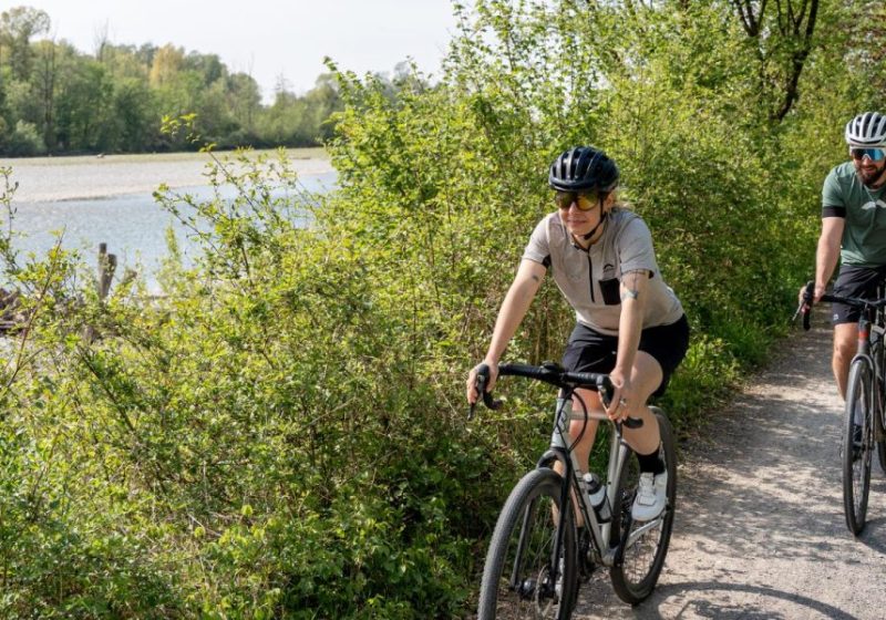 Zwei Gravelbiker - eine Frau und ein Mann - fahren mit Gravelbikes der Bregenzerach entlang, beide tragen einen Fahrradhelm.