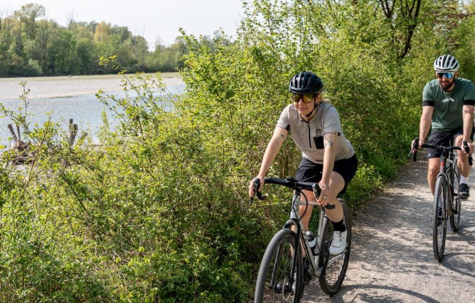 Zwei Gravelbiker - eine Frau und ein Mann - fahren mit Gravelbikes der Bregenzerach entlang, beide tragen einen Fahrradhelm.