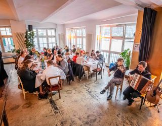 Personen am gedeckten Tisch und zwei Musiker