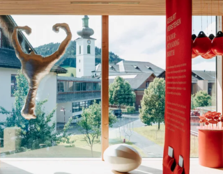 Blick aus dem Frauenmuseum auf das Dorfzentrum mit Pfarrkirche von Hittisau. Im Vordergrund Objekte einer Ausstellung zu sehen.