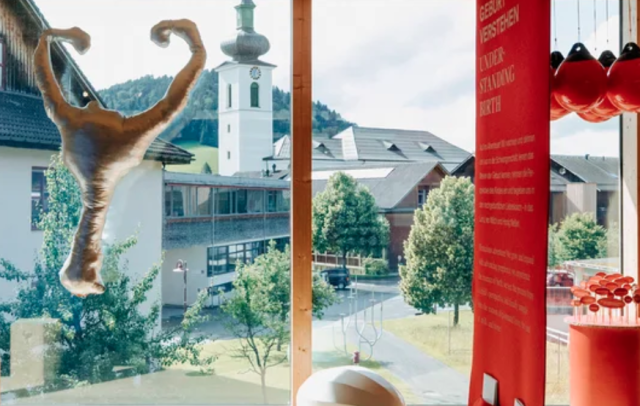 Blick aus dem Frauenmuseum auf das Dorfzentrum mit Pfarrkirche von Hittisau. Im Vordergrund Objekte der Ausstellung geburtskultur. vom gebären und geboren werden. © Frauenmuseum Hittisau / Angela Lamprecht
