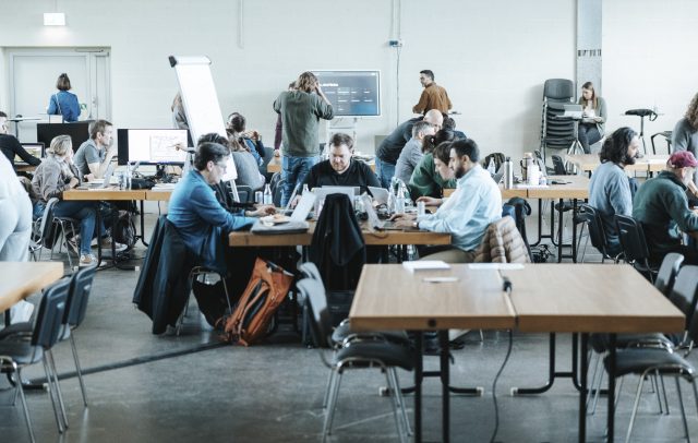Mehrere Gruppen sitzen zusammen und arbeiten beim Hackathon